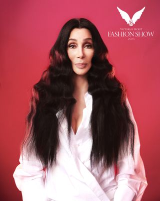 Cher stands in front of a pink backdrop wearing a pink shirt