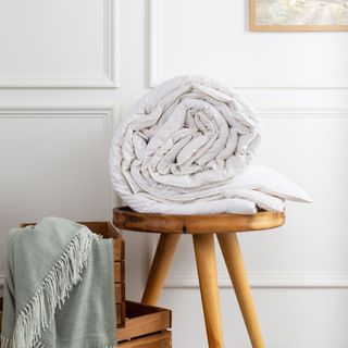 White duvet rolled up on wooden stool