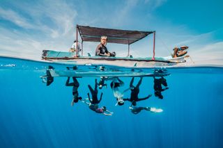 Skilled freedivers hang upside down beneath a boat, defying gravity and basking in their unique moment of underwater grace. Sri Lanka. Ocean Photographer of the Year 2024 finalist