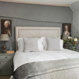 Grey bedroom in a cottage with period style portrait prints on the wall