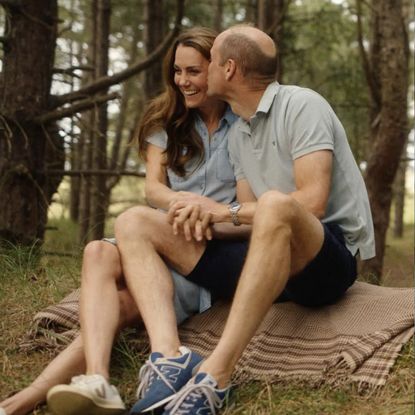 Kate Middleton and Prince William sitting on a blanket kissing in the woods