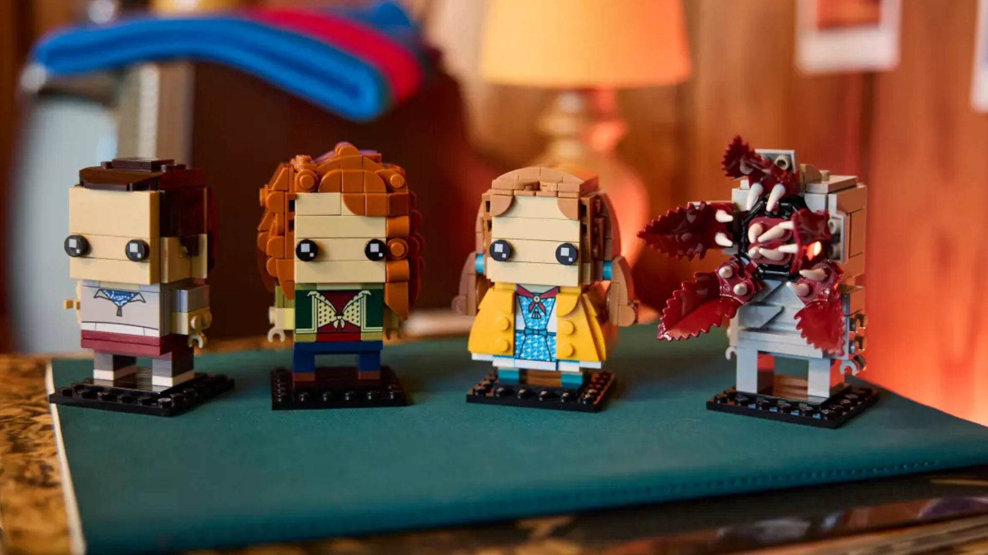 Lego Eleven, Max, Holly, and Demogorgon figures on a green mat in a wood-panelled room