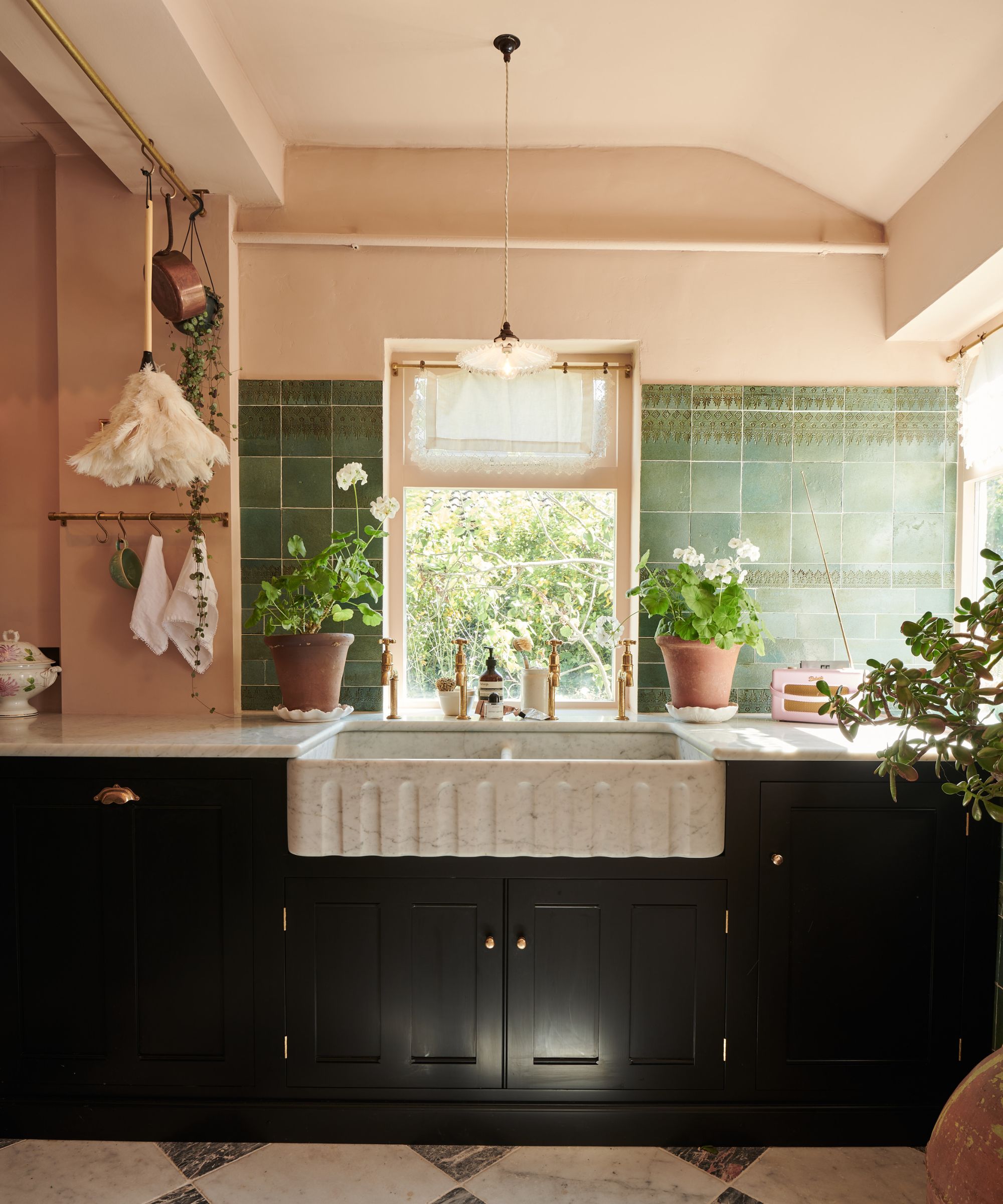 A country kitchen with pink walls, green wall tiles, black cabinetry, and a marble sink