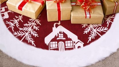 A white house and trees printed on a white tree skirt, surrounded by wrapped presents.