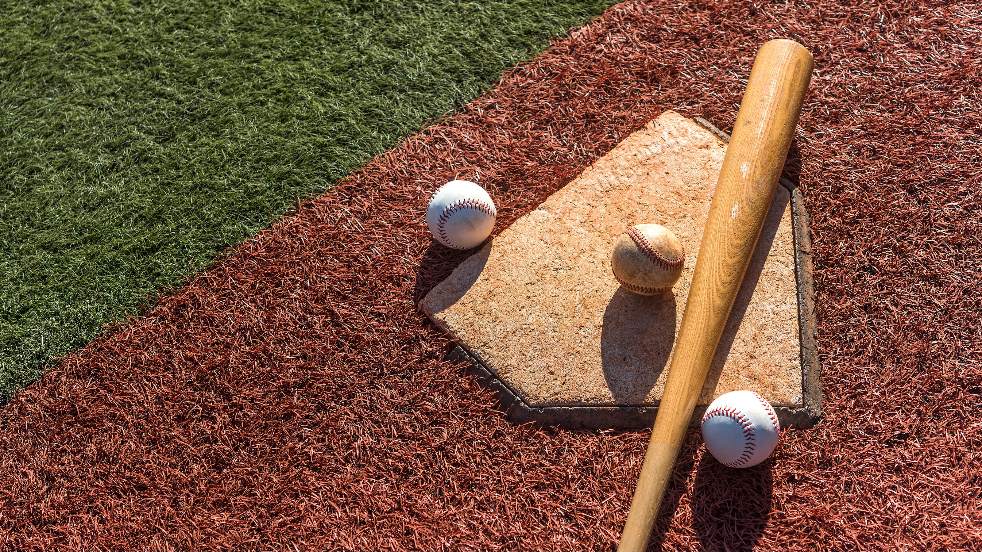 Three baseballs and a bat lying on the home plate of a baseball diamond.