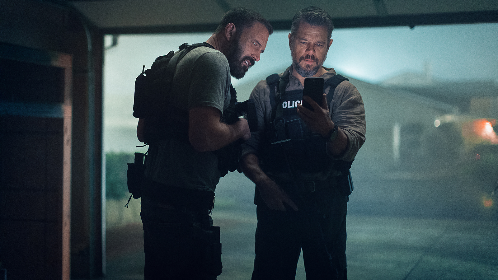 J.D and Dane looking at a mobile phone while standing in a garage at night in Netflix's The RIP