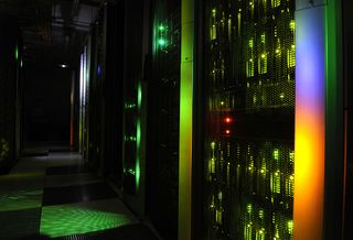 A row of server racks lit in multi-coloured lights in a dark data centre room
