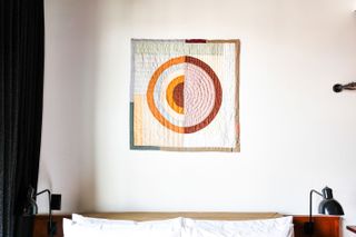 The new Ace Hotel Brooklyn, Thompson Street Project, Kiva Motnyk tapestry artwork on the wall over a bed, white wall, dark grey curtain, wooden double bed frame, black metal bed side lamps