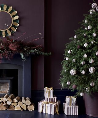 A purple living room with navy fireplace deocrated with a fir garland, a full christmas tree with baubles stands besides