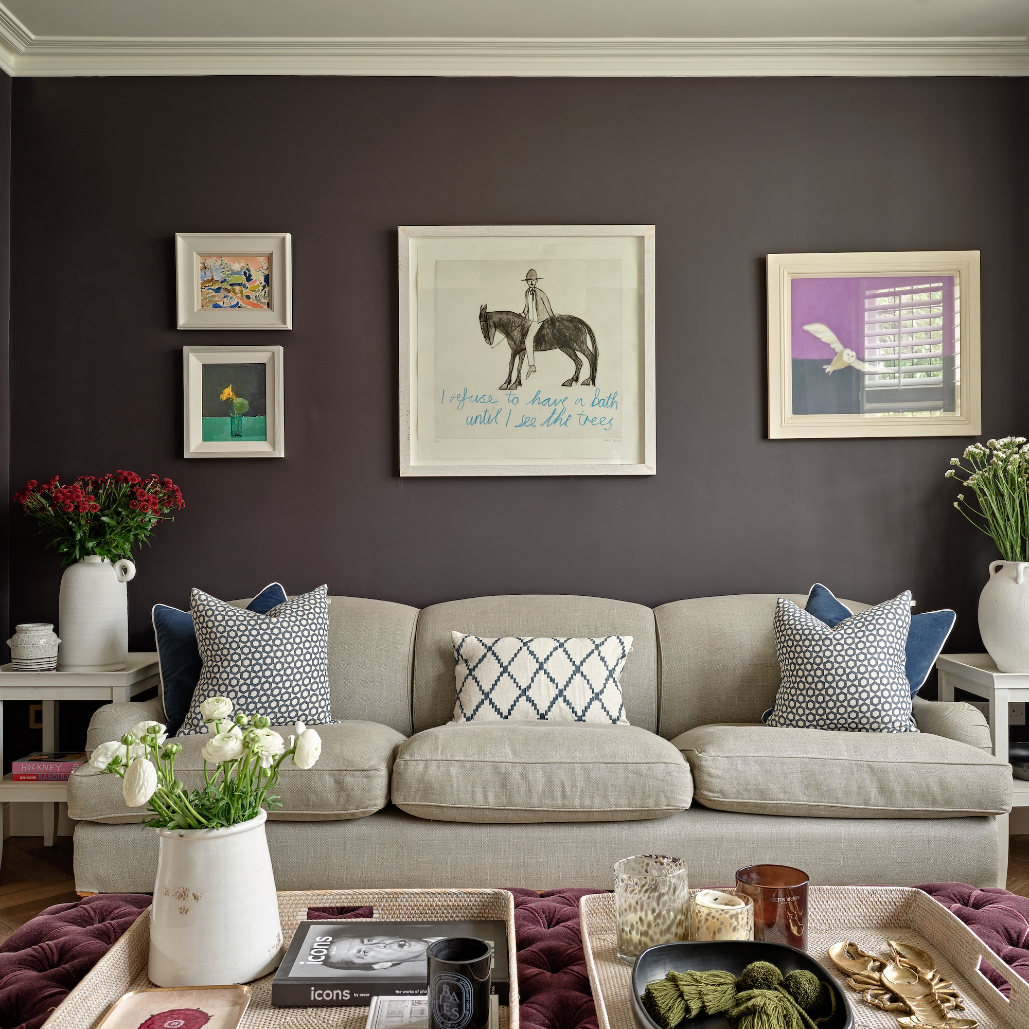 sitting area with black walls, grey sofa, upholstered ottoman coffee table with display trays on top, and gallery wall of contemporary artworks