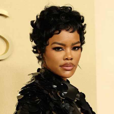 a black woman with short black hair posing on a red carpet in front of a butter yellow background