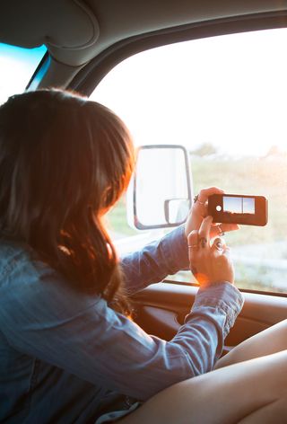 Someone using a phone to take a photo out of a car window