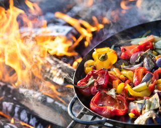 cooking peppers in a grill pan over a fire pit
