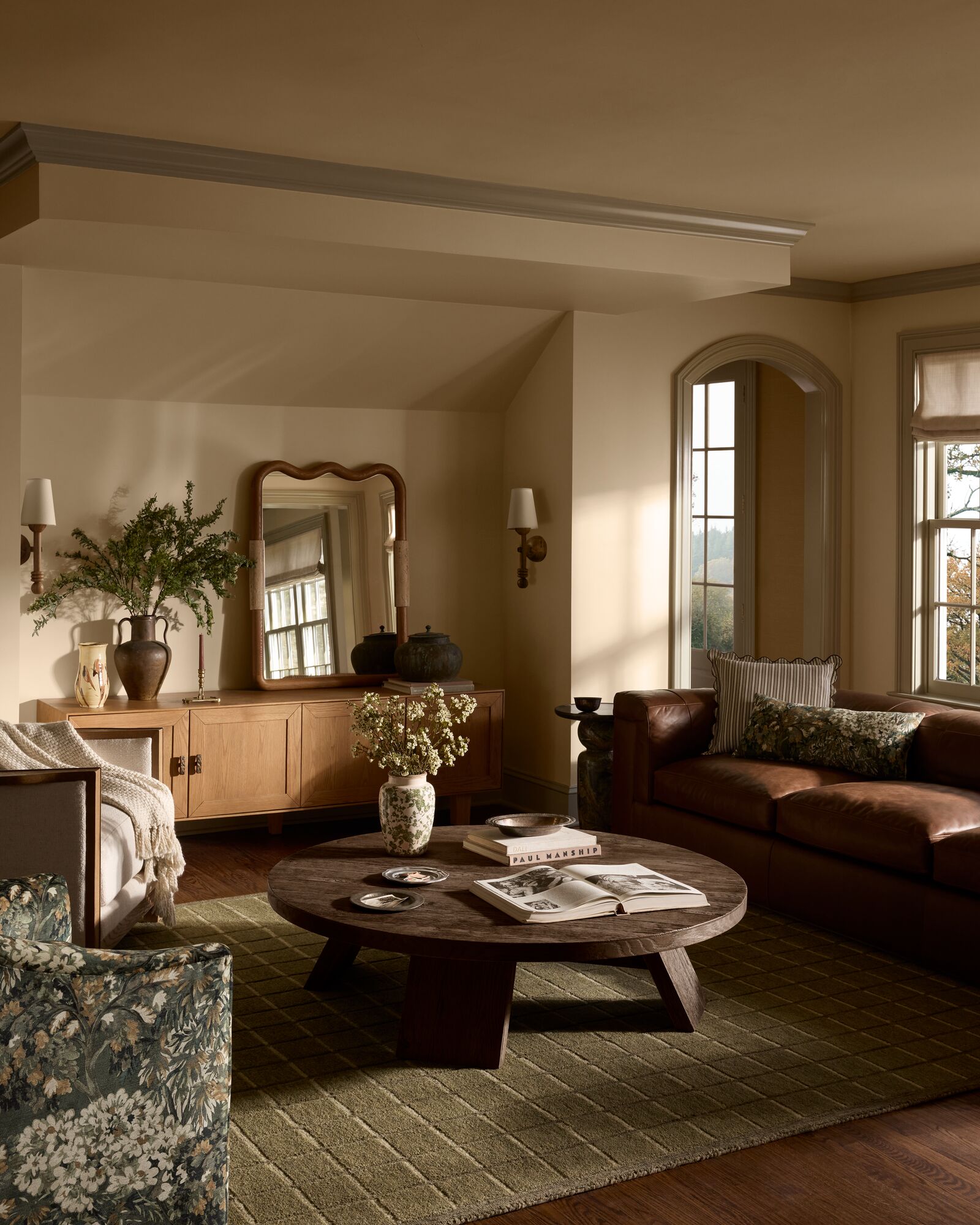 Living room with a green monochromatic geometric rug, circular wooden coffee table, wooden credenza, scalloped edge mirror, and leather sofa