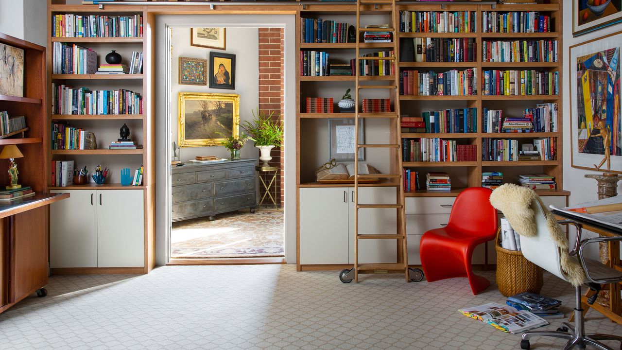 Family living room with busy mid-century bookcase and lightly patterned wall to wall carpet looking through to hallway