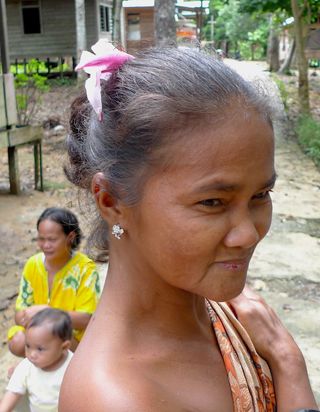 Right profile of an Indonesian woman with gray hair, wearing a brown and orange pattered wrap. 