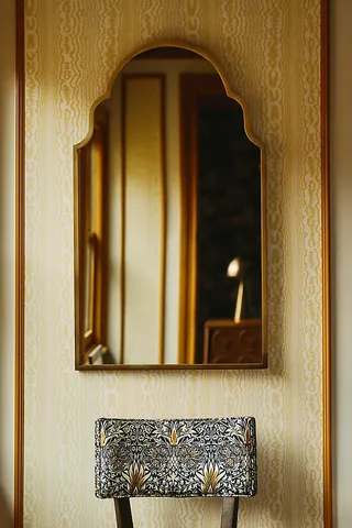 A gold framed mirror with a rectangular base and a curved top, hanging on a wall