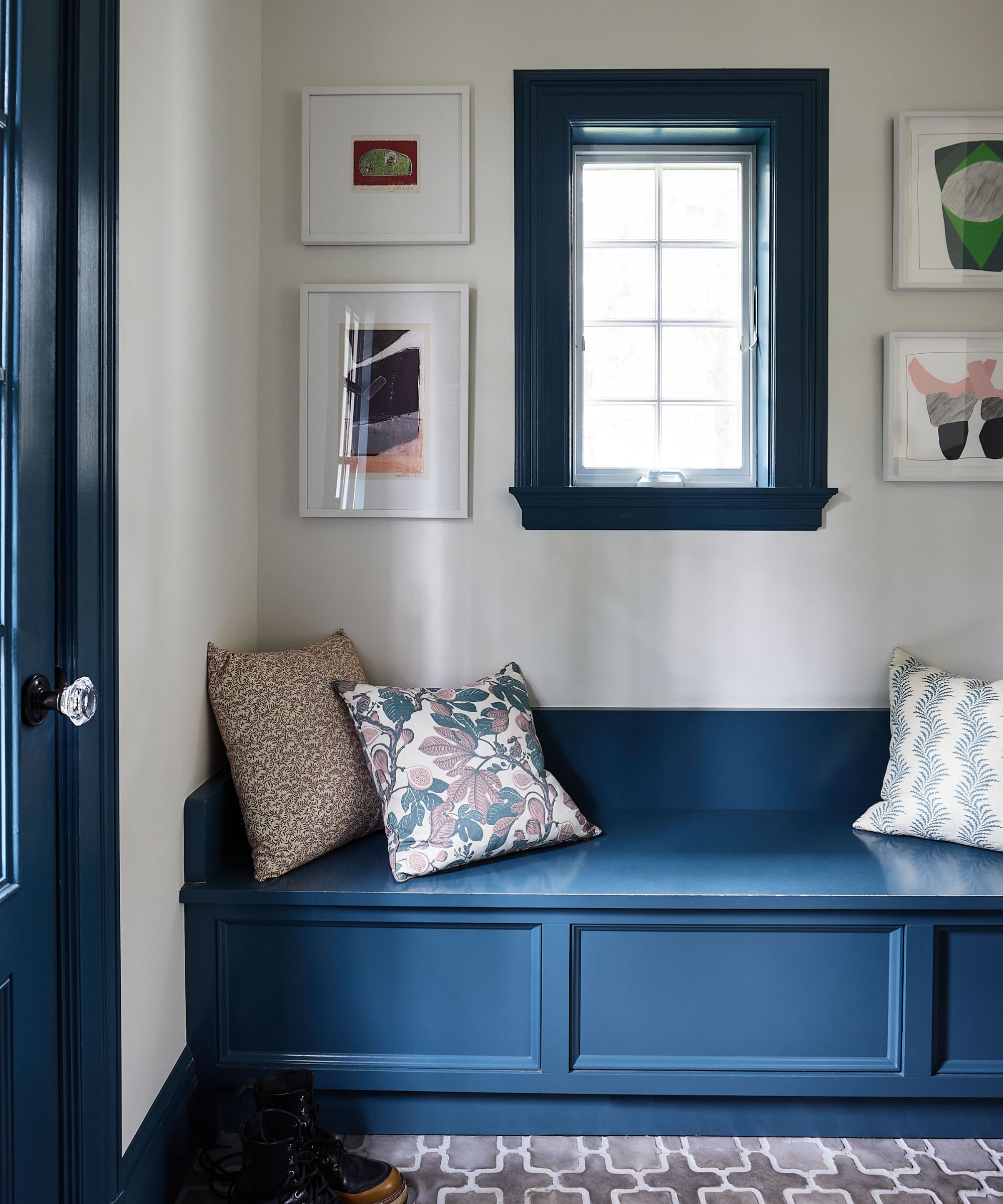 Mudroom with blue painted storage bench and window frame, tiled floor, matching art in white frames and floral cushions