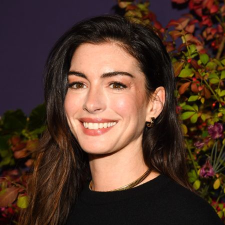 a white woman with dark hair poses in front of a floral backdrop