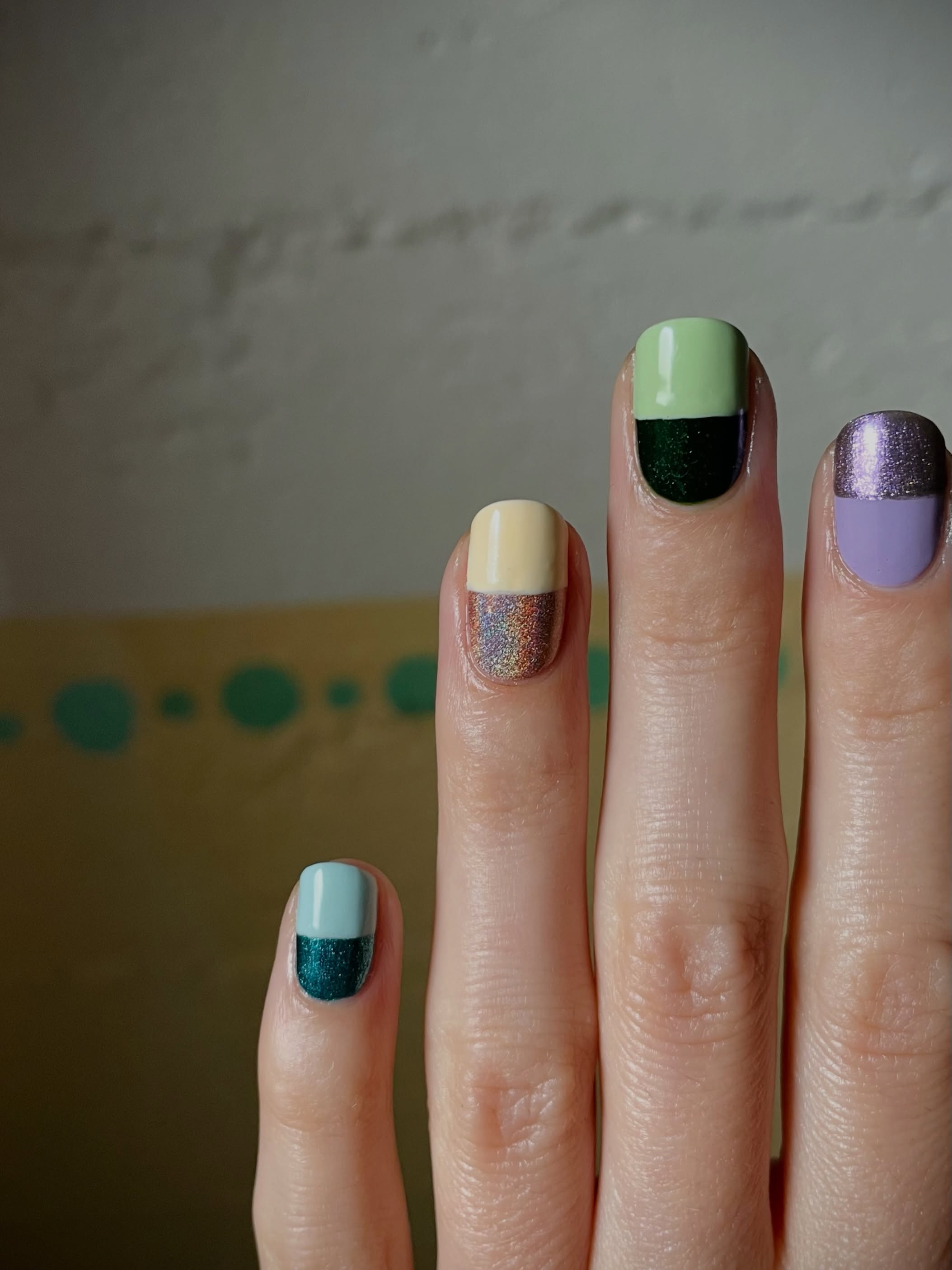 a hand in front of a white wall with four fingers featuring monochromatic nail polishes with glitter shades