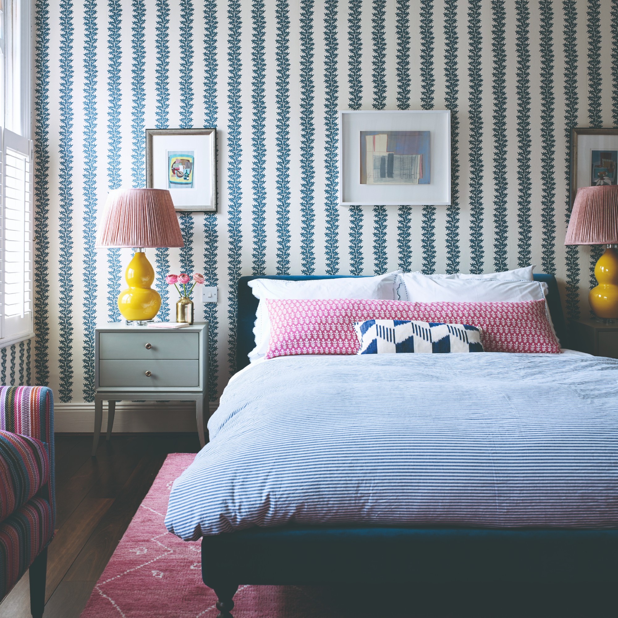 A bedroom with a striped-style floral wallpaper, striped bedding and matching yellow table lamps on bedside tables