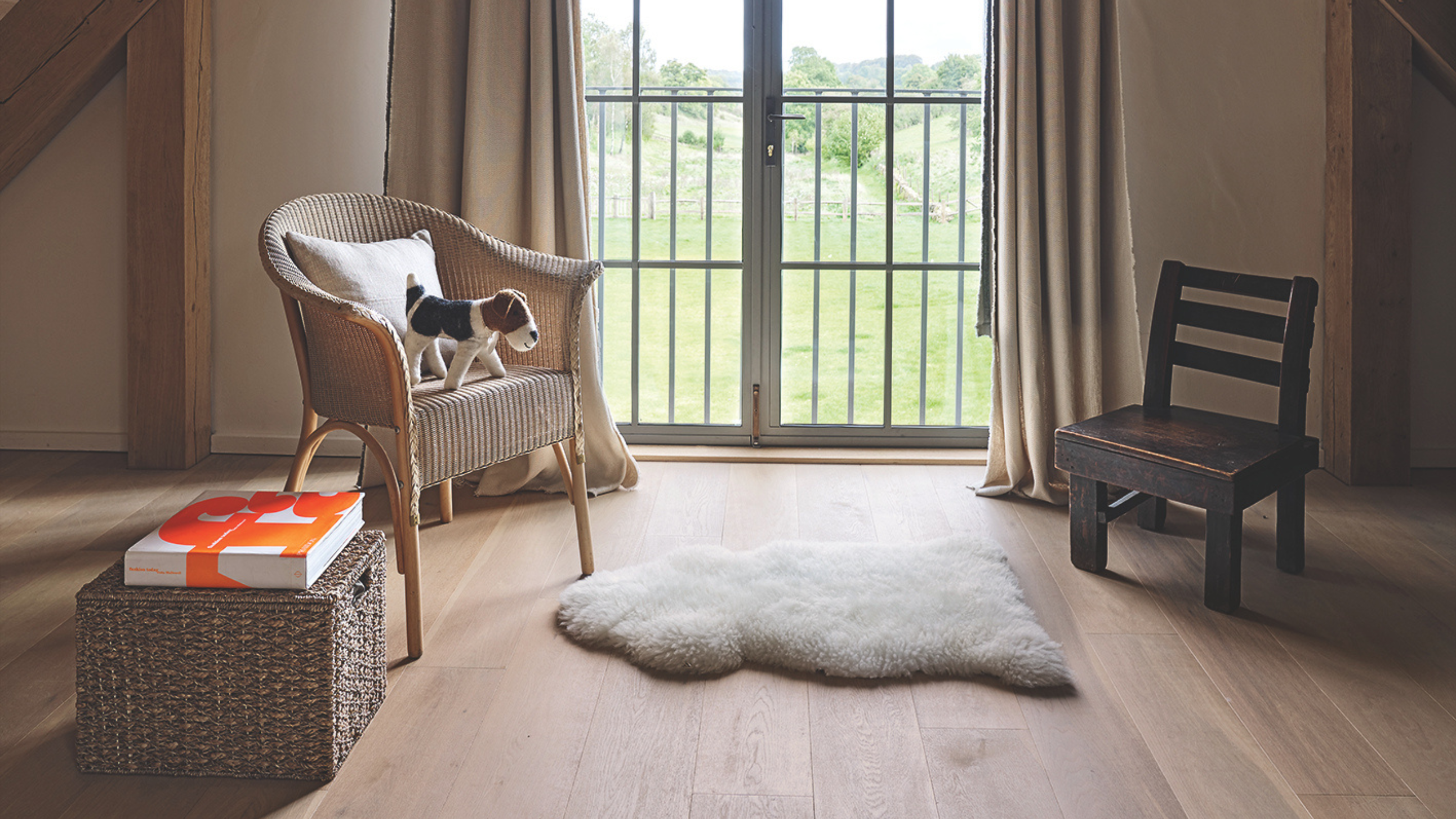 Barn extension decorated with a stylish Scandi feel. Bedroom detail, wicker chair and sheepskin rug at window.