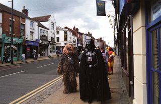 People in costumes from the Star Wars franchise are walking down the street.
