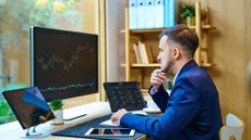 A man looks at trading graphs on computer monitors on his desk.
