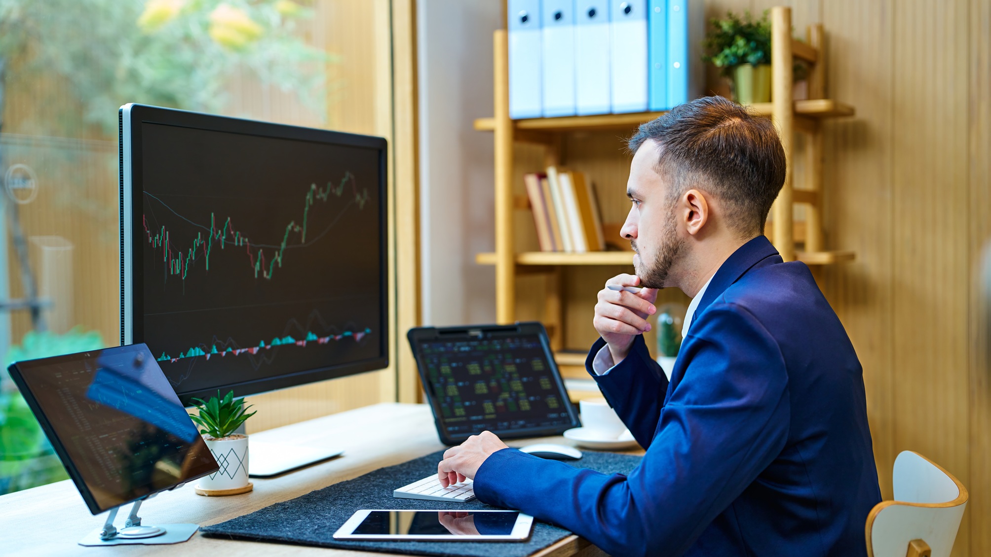 A man looks at trading graphs on computer monitors on his desk.