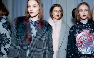 Four female models wearing looks from MSGM's collection. One model is wearing a grey piece with dark blue floral design. Next to her is a model wearing a grey shirt with blue floral design and a black and white checked houndstooth coat with blue and red fur. The third model is wearing a grey coat and pink fluffy scarf. And the fourth model is wearing a light blue shirt and dark blue hoodie with multicoloured design
