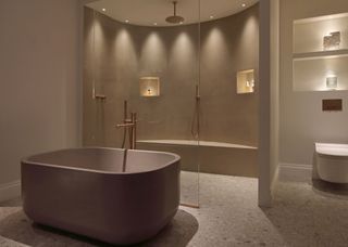 A large bath tub in the middle of a bathroom with a large shower. There are neutral tones throughout the room and spotlights dotted around the bathroom shower.