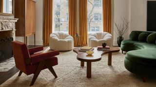 A living room with yellow floor-length curtains against two windows, a green curved sofa, three armchairs, with a sculptural coffee table and freestanding storage unit in a corner