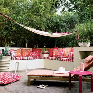 Built-in corner seating with pink and orange patterned cushions on wooden decking area in garden