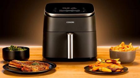 A COSORI TurboBlaze air fryer with a selection of prepared foods including steak, fries, and, vegetables on wooden surface