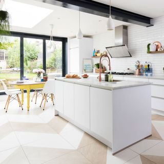 white kitchen with a white island and a kitchen sink with a brass kitchen tap and a gas stove, next to a wooden yellow table with white chairs with wooden legs decorated with flowers