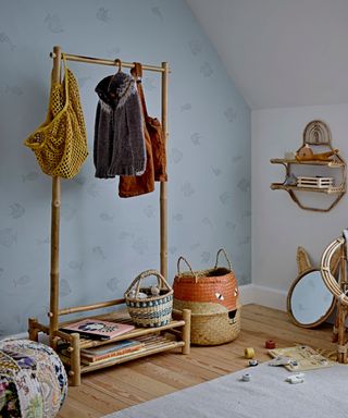 A blue bedroom with a bamboo clothing rack with costs on and a storage basket