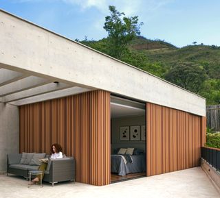 Covered outdoor seating and glimpse of bedroom at Casa Prática by Estúdio Zargos