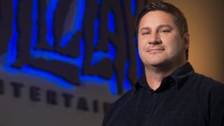 Deceased Blizzard art director Bill Petras standing in front of a Blizzard logo.