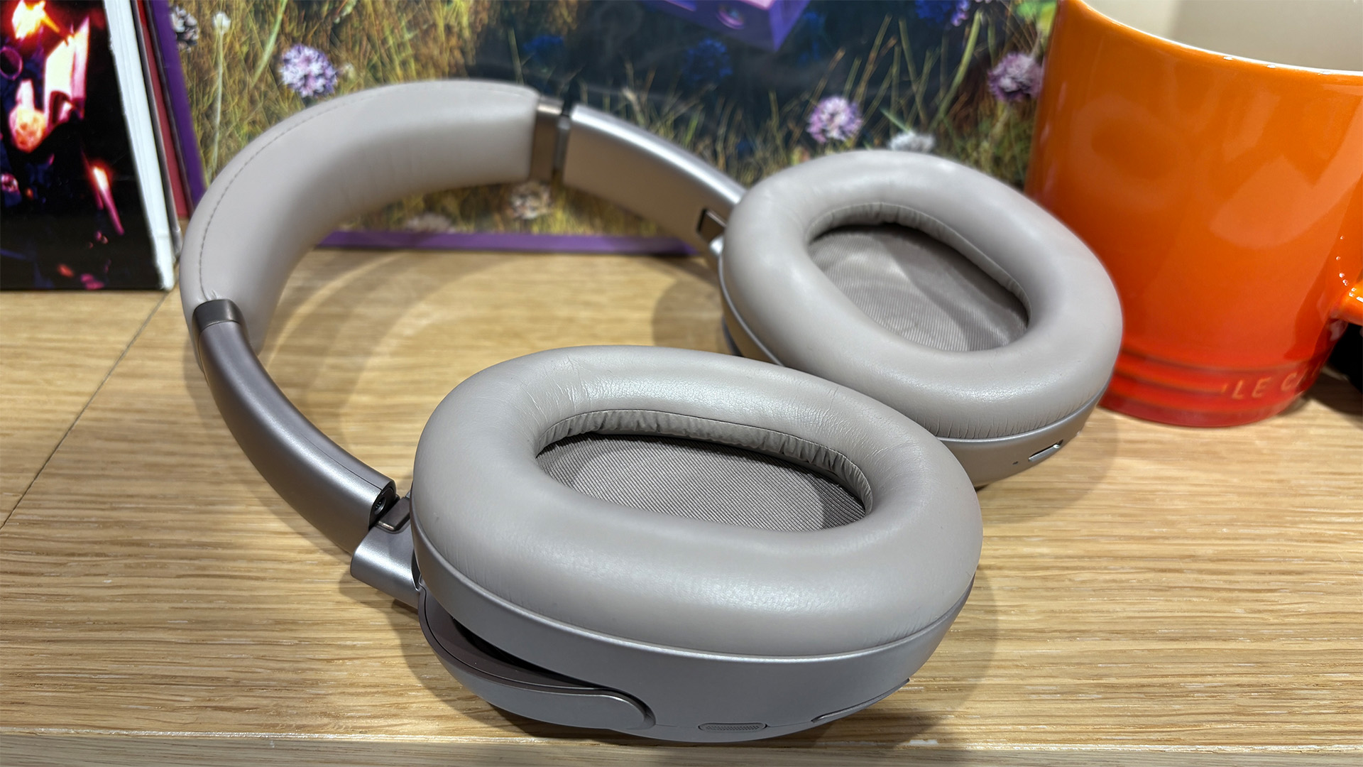 JBL Tour One M3 Smart Tx wireless over-ear headphones laid flat on busy bookshelf