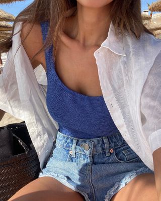 Marianne Smyth wears a Hunza G swimsuit, denim shorts and a white button up.