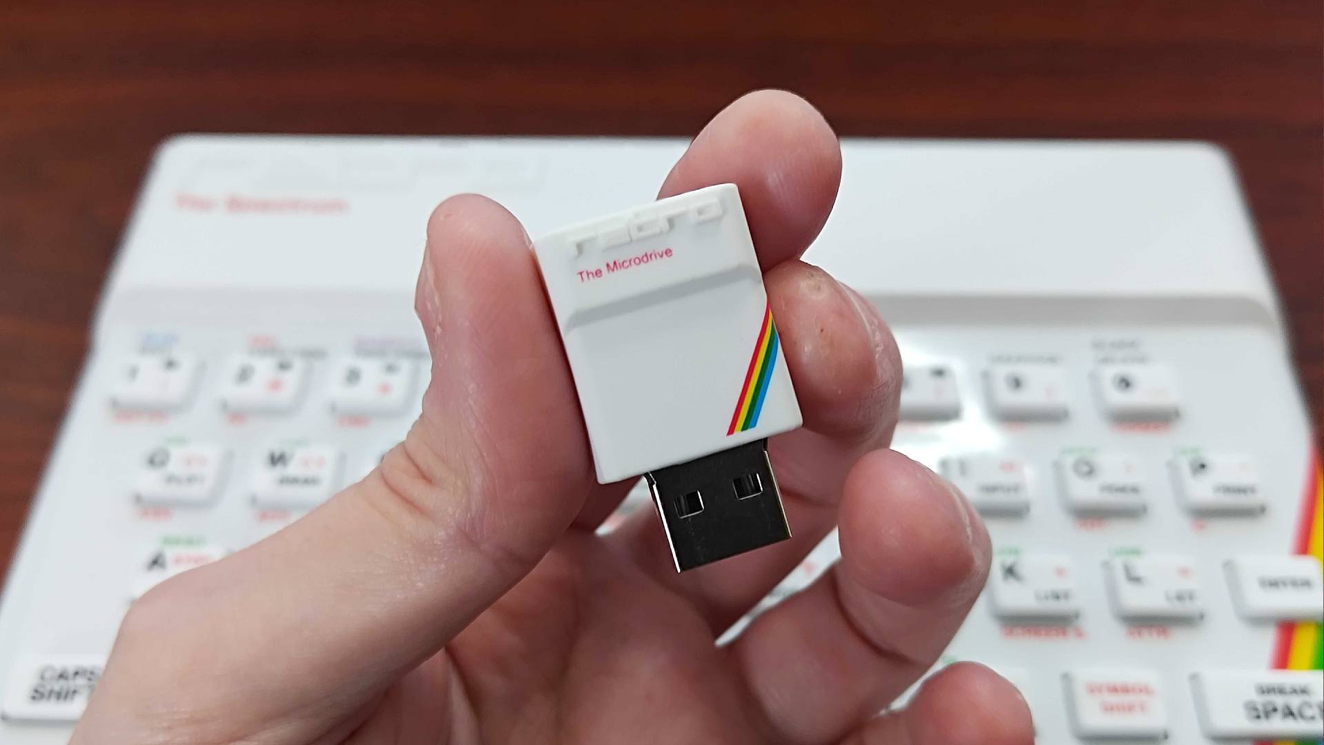 Hand holding "The Microdrive" USB stick in front o The Spectrum White Edition.