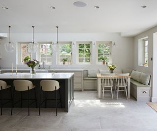 Bright shaker-style kitchen featuring built-in banquette seating, a wooden dining table, neutral cabinetry, and a spacious island with elegant pendant lighting.