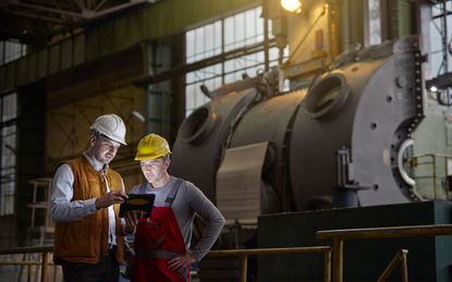 Male engineer and worker using digital tablet in dark factory