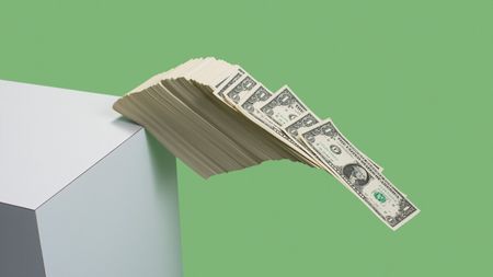 Stack of US $1 bills fall over edge of white shelf on green background