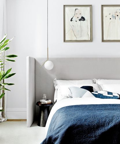 Modern bedroom lighting tips with a gray statement headboard and artwork on white walls.