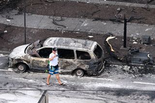 An aerial image taken on August 10, 2023 shows a person walking past a destroyed car in the aftermath of wildfires in western Maui in Lahaina, Hawaii.