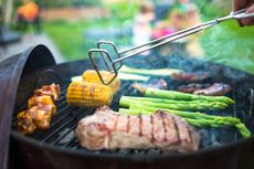 An example of charcoal grills safety - tongs cooking pork and vegetables on white-hot flames