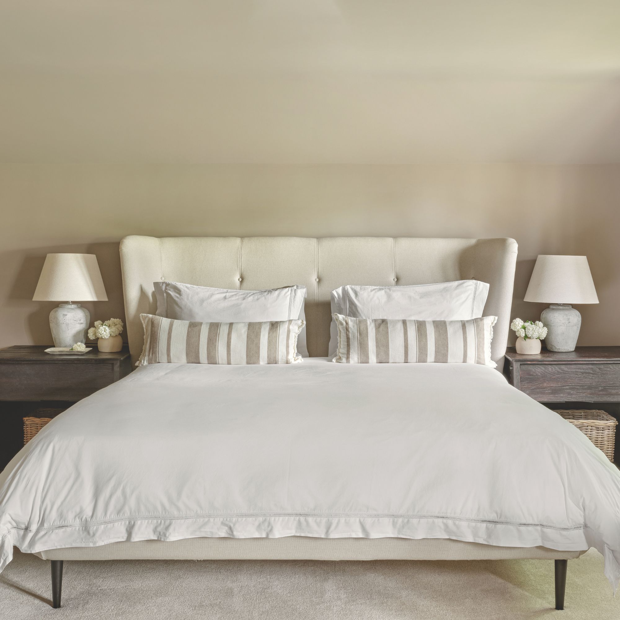 Main bedroom with light coloured buttoned headboard, dark beige walls, dark wood bedside tables and matching table lamps