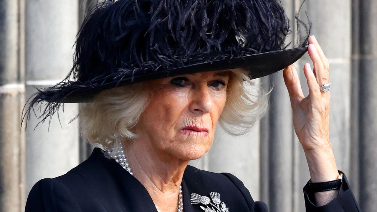 Queen Camilla wears a feathery black hat and looks sad