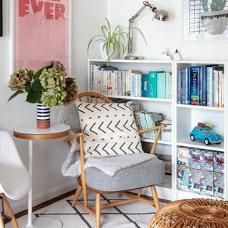 A living room with a low white bookcase displaying a toy car with two lounge chairs and a side table next to it